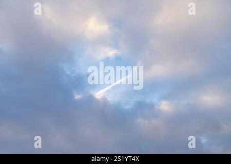 Traînée de condensation d'un avion à réaction coupant à travers les nuages de cirrus dans un ciel bleu vif. La piste de l'avion s'étend à travers l'atmosphère, lea Banque D'Images