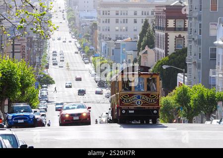 San Francisco, CA, États-Unis. 24 avril 2012 : tramway rouge historique voyageant en montée sur une rue ensoleillée de San Francisco. Banque D'Images
