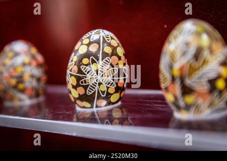 Trois œufs peints sont exposés sur une étagère. Les œufs sont décorés de différentes couleurs et motifs, y compris des fleurs et des points. La disposition de t Banque D'Images