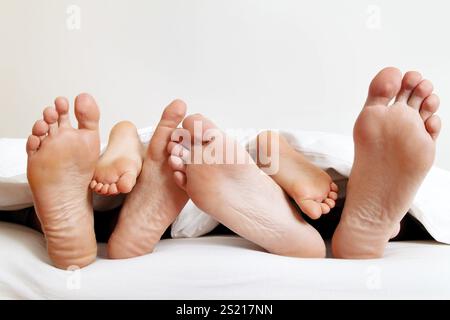 La plante des pieds d'une famille au lit sous les couvertures. Autriche Banque D'Images