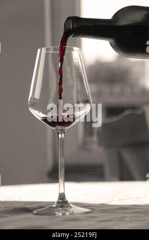 Verser le vin rouge de la bouteille dans un verre à vin en noir et blanc Banque D'Images