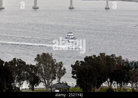 San Diego, Californie, États-Unis. 22 décembre 2024. Deux élégants yachts de loisirs naviguent sur les eaux calmes de la baie de San Diego, en passant sous l'emblématique pont Coronado. Le premier plan comprend un parc serein avec des arbres luxuriants et un petit pavillon, créant un contraste entre l'activité sur l'eau et le cadre paisible du rivage. Les yachts laissent des sillons subtils alors qu'ils glissent sans effort à travers la baie. (Crédit image : © Ian L. Sitren/ZUMA Press Wire) USAGE ÉDITORIAL SEULEMENT! Non destiné à UN USAGE commercial ! Banque D'Images