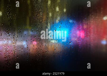 Gouttes de pluie sur la fenêtre en verre de pare-brise avec bokeh de lumière de route, vie nocturne de ville de lumière colorée dans un fond abstrait de jour de pluie, goutte d'eau sur le verre Banque D'Images