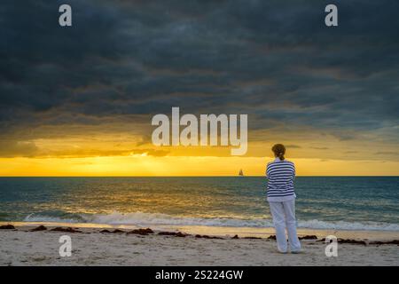 Une femme regarde le coucher du soleil sur la plage de Naples, en Floride Banque D'Images