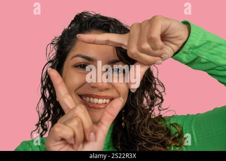 Femme souriante encadrant son visage avec les doigts, exprimant la créativité et l'attitude positive Banque D'Images