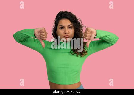 Jeune femme montrant un geste du pouce vers le bas exprimant l'aversion, la désapprobation, le désaccord ou la rétroaction négative sur fond rose Banque D'Images