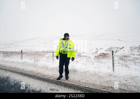 Un policier se tient dans la neige après avoir aidé à dégager des voitures d'une dérive de neige à Ribblehead, dans le North Yorkshire. De grandes parties du Royaume-Uni sont confrontées à de fortes chutes de neige et à des pluies verglaçantes, ce qui est susceptible de causer des perturbations, après l'entrée en vigueur de deux avertissements météorologiques jaunes. Des véhicules bloqués sur les routes, des voyages ferroviaires et aériens retardés ou annulés, et des coupures de courant sont tous probables alors que le pays est aux prises avec une période hivernale d'une semaine, a déclaré le met Office. Date de la photo : lundi 6 janvier 2025. Banque D'Images