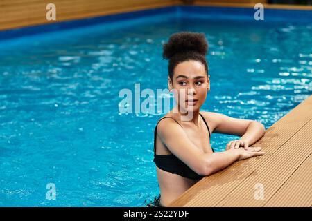 Une jeune femme afro-américaine se penche contre le bord de la piscine, embrassant détente et calme. Banque D'Images