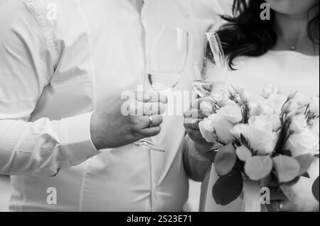 Toast de mariage romantique avec mariée et mariée tenant des verres à champagne et un bouquet de mariée. Banque D'Images