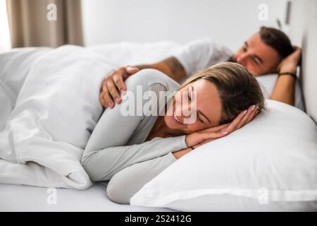 Jeune couple marié s'embrassant dans leur lit. Ils se détendent après le travail dans l'après-midi. Banque D'Images