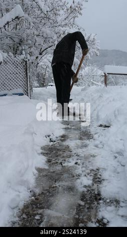 homme de derrière dans des vêtements noirs dégageant le chemin entre les déneiges dans la cour arrière ou le jardin après la tempête de neige, travail saisonnier d'hiver dans la zone rurale Banque D'Images