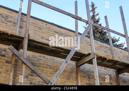 Un échafaudage en bois s'élève contre un mur de briques, aidant aux efforts de rénovation par temps clair avec quelques arbres visibles en arrière-plan. Banque D'Images