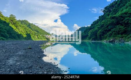 Une vue imprenable sur une rivière calme et turquoise reflétant le ciel et les montagnes verdoyantes. Un pont est visible au loin. Situé dans le quartier de Wulai Banque D'Images