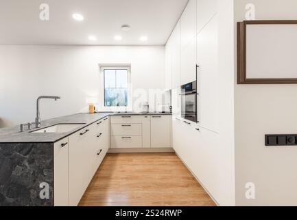 Cuisine lumineuse et contemporaine dotée d'armoires blanches, d'un élégant dosseret et d'un agencement spacieux avec vue sur la fenêtre. Idéal pour les maisons modernes et Banque D'Images