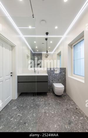 Salle de bains contemporaine avec carrelage gris, meuble-lavabo gris minimaliste, murs blancs et éclairage d'ambiance encastré pour un look épuré et élégant Banque D'Images