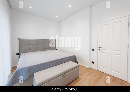 Chambre contemporaine avec parure de lit simple mais élégante grise, lit simple moderne, lumière naturelle à travers des rideaux transparents et murs lumineux Banque D'Images