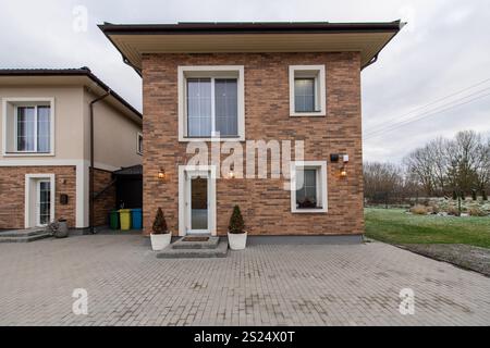 Façade élégante d'une maison en brique de deux étages dans une allée de quartier de banlieue bien entretenue, accents d'éclairage chaleureux, toile de fond sereine de verdure. Le Banque D'Images