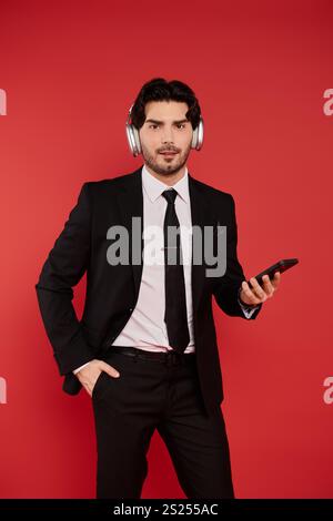 Un jeune homme élégant aux cheveux bruns écoute en toute confiance de la musique sur son smartphone. Banque D'Images