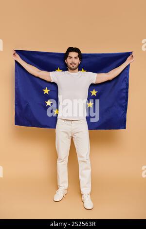 Un jeune homme aux cheveux bruns se tient confiant, affichant avec fierté le drapeau de l'Union européenne. Banque D'Images