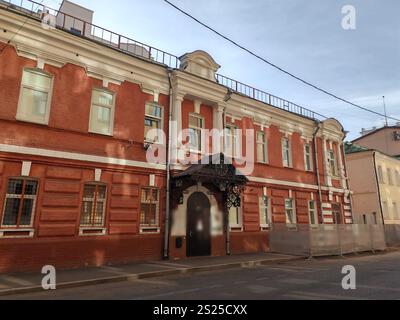 Un bâtiment en briques rouges avec des colonnes blanches contrastées, des fenêtres barrées et un auvent d'entrée noir décoratif. La photo capture la beauté intemporelle de Banque D'Images