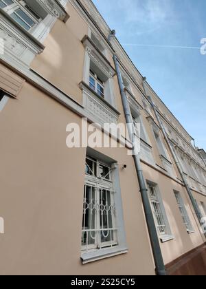 Une rue étroite de la ville avec un bâtiment résidentiel beige avec des fenêtres barrées et des tuyaux métalliques. L'image souligne la géométrie urbaine et le contraste Banque D'Images