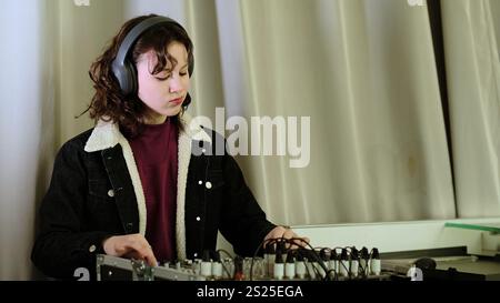 Une fille se penche sur une table d'harmonie, ses mains sur les commandes et un sourire sur son visage. Cette image capture la joie de l'implication créative dans la musique ou Banque D'Images