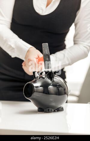 Young businesswoman hitting piggy bank with hammer Banque D'Images