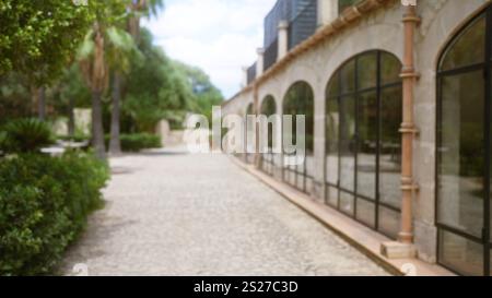 Scène extérieure floue à majorque avec un chemin pavé, des fenêtres cintrées, une végétation luxuriante et une architecture méditerranéenne avec un ciel lumineux et déf Banque D'Images