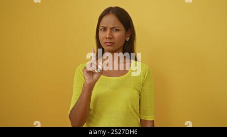 Jeune femme hispanique debout sur fond jaune isolé avec une expression sérieuse tenant l'index vers le haut indiquant la prudence ou des conseils Banque D'Images