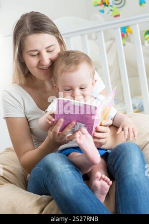 Portrait de bébé garçon assis sur les genoux des mères et livre de lecture Banque D'Images