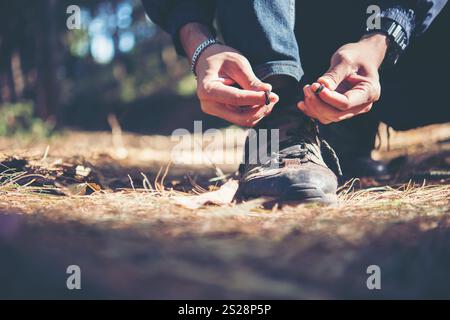 Jeune homme randonneur les lacets étroits sur sa chaussure lors d'une maison de grande randonnée pédestre en forêt. Banque D'Images