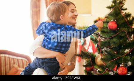 Portrait de belle mère embrassant son garçon tout-petit et décorant l'arbre de Noël Banque D'Images