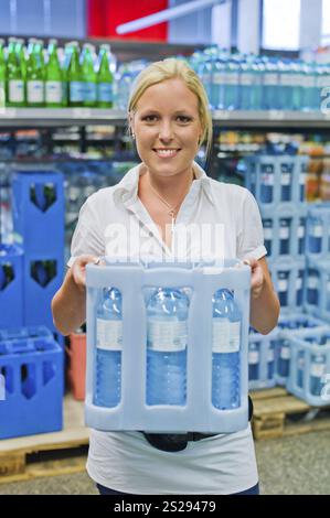 Une jeune femme achète de l'eau minérale dans la section boissons du supermarché. Autriche Banque D'Images