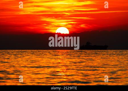 Bateau paisible flotte sur l'eau calme, baigné dans les couleurs vives d'un coucher de soleil. La scène sereine capture la beauté de la nature, avec des teintes chaudes reflétant Banque D'Images
