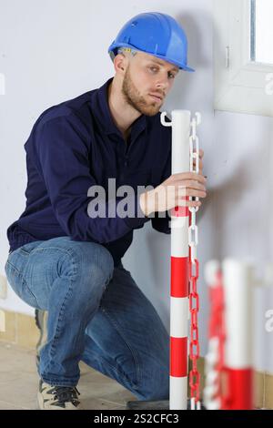 jeune ouvrier masculin érigeant une chaîne de sécurité autour du site Banque D'Images