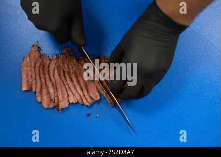 Vue aérienne rapprochée d'un homme tranchant de la viande sur une planche à découper bleue Banque D'Images