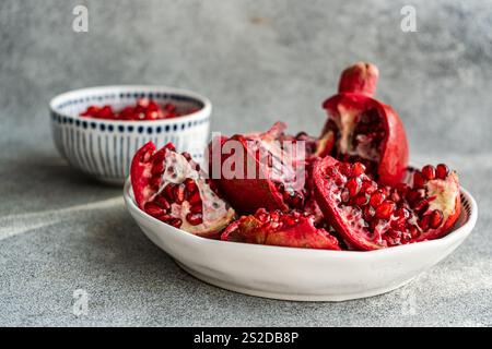 Gros plan d'un plat de grenades fraîches ouvertes sur une table avec un bol de graines de grenade Banque D'Images