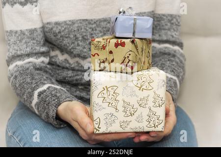 Une personne tient trois cadeaux magnifiquement emballés dans du papier de fête, mettant en valeur l'esprit des fêtes lors d'une réunion intérieure confortable. Banque D'Images