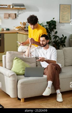 Deux hommes partagent un moment d'amour tout en s'engageant avec leurs appareils dans une maison élégante. Banque D'Images