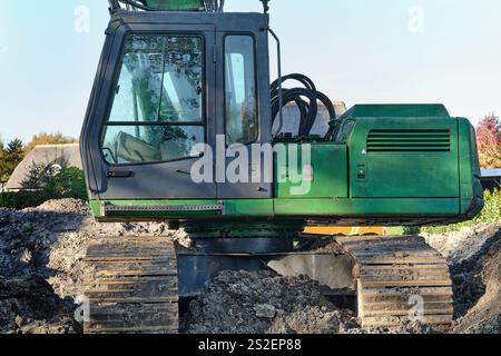 Vue latérale sur une excavatrice verte fonctionne sur un chantier de construction où une nouvelle maison résidentielle est en construction. Banque D'Images