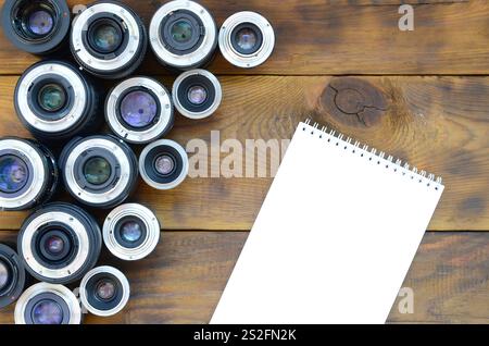 Plusieurs objectifs photographiques et un carnet blanc sont situés sur un fond en bois marron. Espace pour le texte Banque D'Images