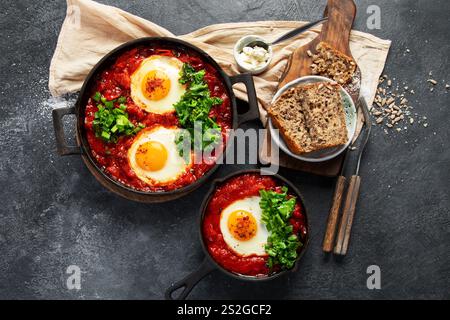 Oeufs Shakshuka dans une casserole avec du pain sur un fond sombre. Oeufs pochés dans une sauce épicée au poivre tomate. Œufs brouillés juifs traditionnels. Vue de dessus. Banque D'Images