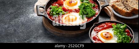 Oeufs Shakshuka dans une casserole avec du pain sur un fond sombre. Oeufs pochés dans une sauce épicée au poivre tomate. Œufs brouillés juifs traditionnels. Vue de dessus. PA Banque D'Images