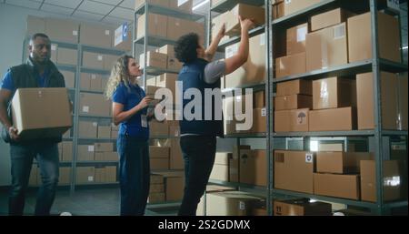 L'associé d'entrepôt masculin met la boîte en carton avec des marchandises sur l'étagère. Gestionnaire d'inventaire féminin utilise un ordinateur tablette, scanne le code sur le colis. Centre de distribution logistique avec commandes en ligne E-commerce. Banque D'Images