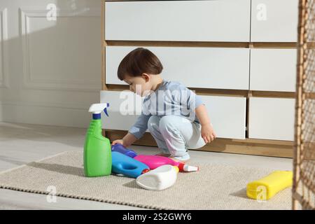 Petit garçon jouant avec des bouteilles de détergents près de l'armoire à la maison. Enfant en danger Banque D'Images