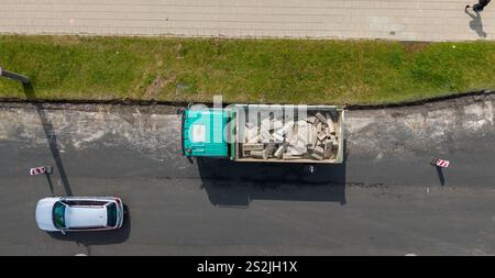 Vue aérienne d'un camion à benne verte chargé de débris de construction stationnés dans une rue. La zone environnante comprend un trottoir et un visi partiel Banque D'Images