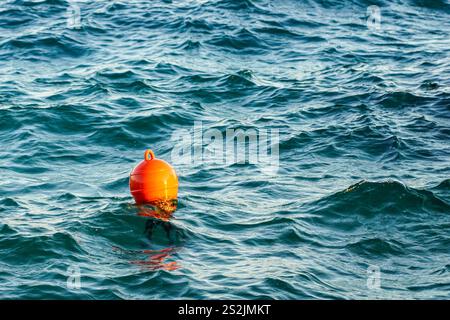 Bouée d'eau en plastique orange flottant dans l'eau de mer turquoise, toile de fond ondulée Banque D'Images
