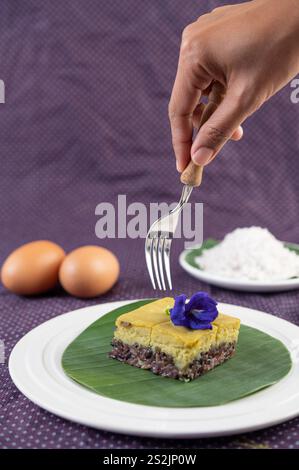 Le manche d'une fourchette qui est sur le point d'insérer le dessert de riz collant noir avec crème anglaise sur la feuille de banane. Banque D'Images