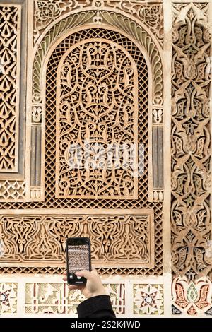 Un touriste photographie les détails d'un mur orné à Marrakech, Maroc. Le motif complexe est un exemple de plâtre Tadelakt. Banque D'Images