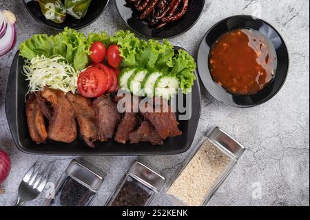 Porc frit garni de sésame, avec tomates, concombres, chou et laitue placés dans un plat noir. Banque D'Images